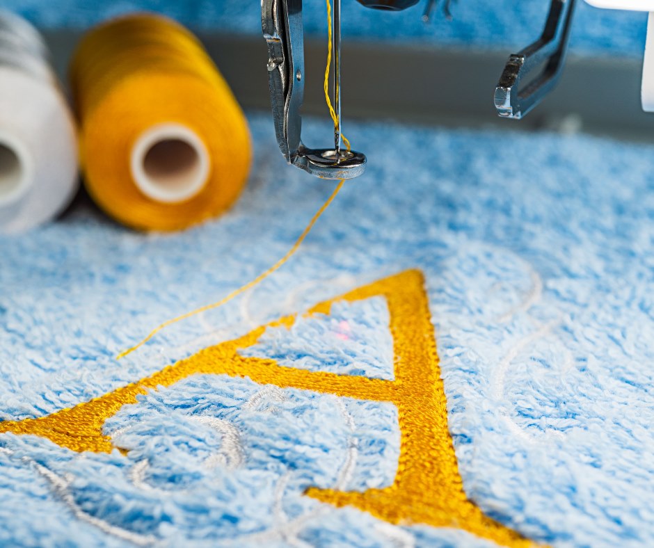 A machine embroidering a golden "A" on some blue fabric